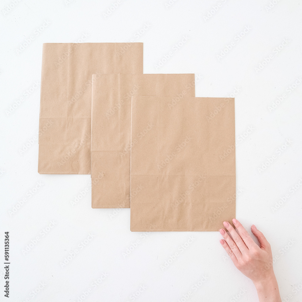 Fototapeta premium Craft bags on a white background with a hand. Place for text and logo. Top view. The concept of packaging, delivery, food.
