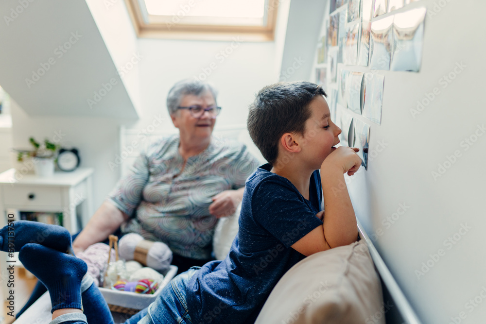 A school-age boy looks at photos taped to the wall, in a cozy room at home, side view A school-age boy looks at photos taped to the wall, in a cozy room at home, side view