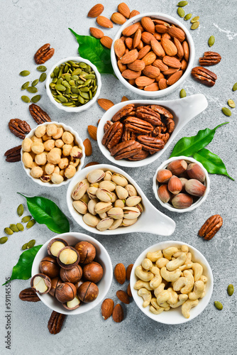 Assortment of nuts in bowls. A variety of peeled nuts on a stone background. Top view.