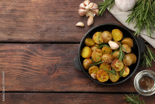 Delicious baked potatoes with rosemary and ingredients on wooden table, flat lay. Space for text
