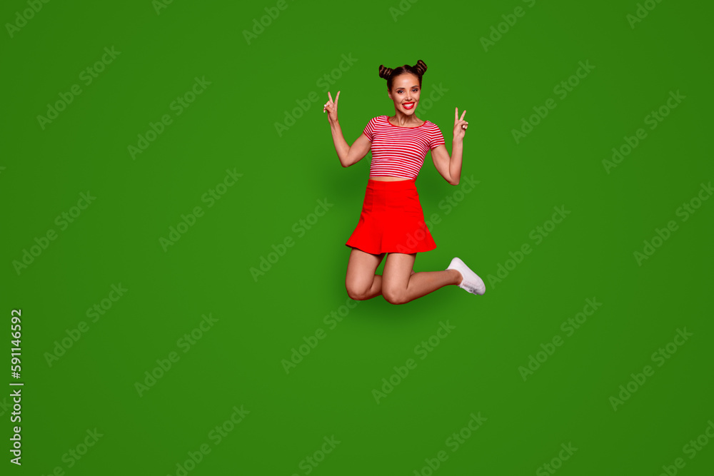 Full-length full-size view of jumping laughing and pretty woman dressed in colourful bright clothes shows a v-sign isolated on red background. Joy fun concept Full-length full-size view of jumping laughing and pretty woman dressed in colourful bright clothes shows a v-sign isolated on red background. Joy fun concept