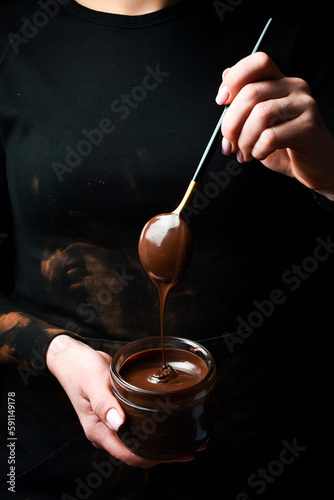 Hot chocolate. Female hands hold a spoon with melted chocolate. Kitchen utensils. On a black background.