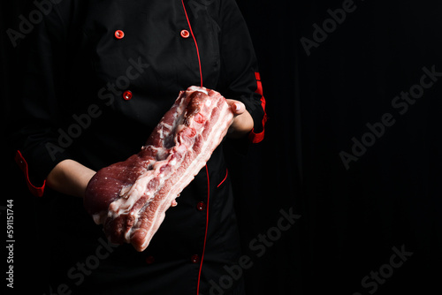 The chef holds a piece of pork belly meat in his hands. On a black background.