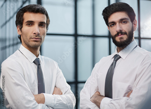 Two serious young businessmen standing with in office