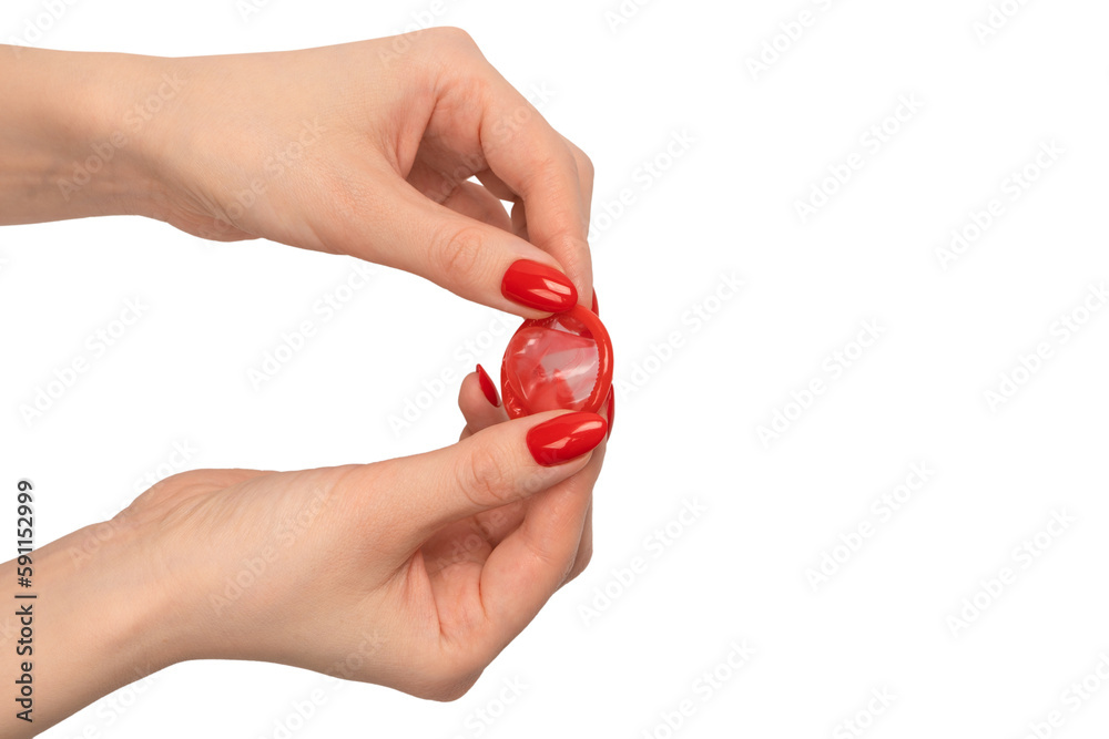 A red condom in a woman hand with red nails isolated on white background. A red condom in a woman hand with red nails isolated on white background.