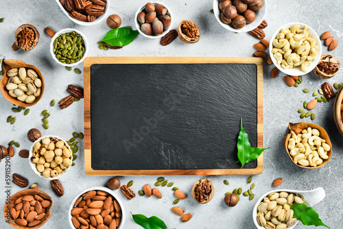 A slate board and a set of nuts in a bowl on a light stone background. Free space for text. Healthy snacks. Nuts