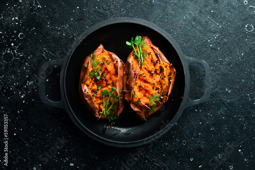 Vegetarian menu. Baked sweet potatoes with spices and garlic in a pan. Healthy food. On a black stone background.