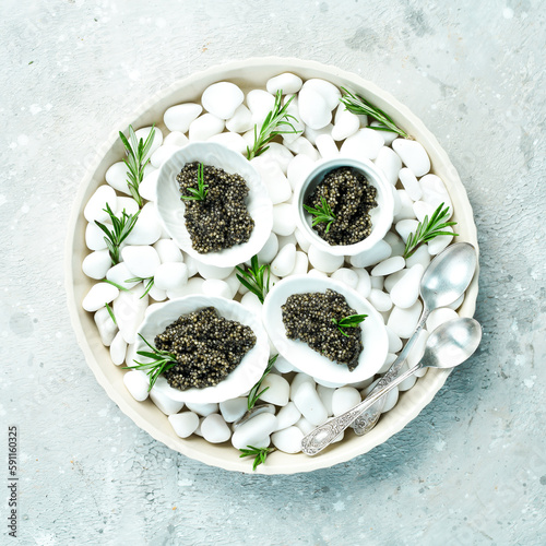 Black caviar in a bowl on chilled white stones. On a gray concrete photo. Top view.