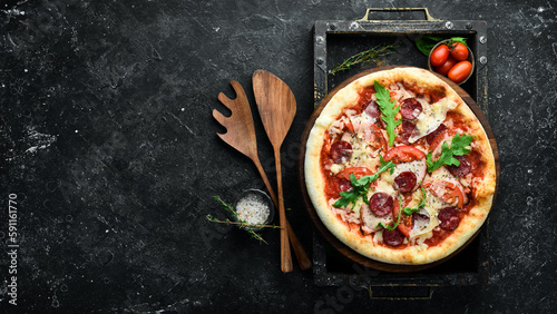 Homemade pizza: sausages, bacon and tomatoes. Takeaway food. Home delivery of food. On a black stone background.