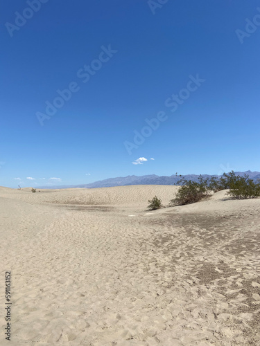 The Mesquite Flat Sand Dunes, mountains, and blue sky in Death Valley National Park, California, USA.