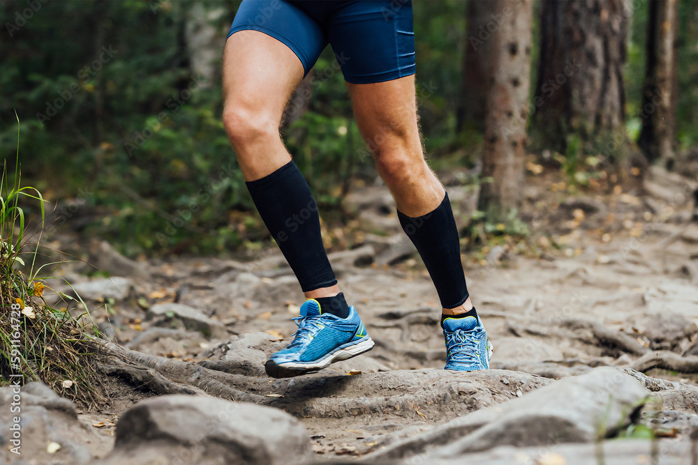 legs runner in compression sleeves on his feet run forest trail race over stones, summer marathon race