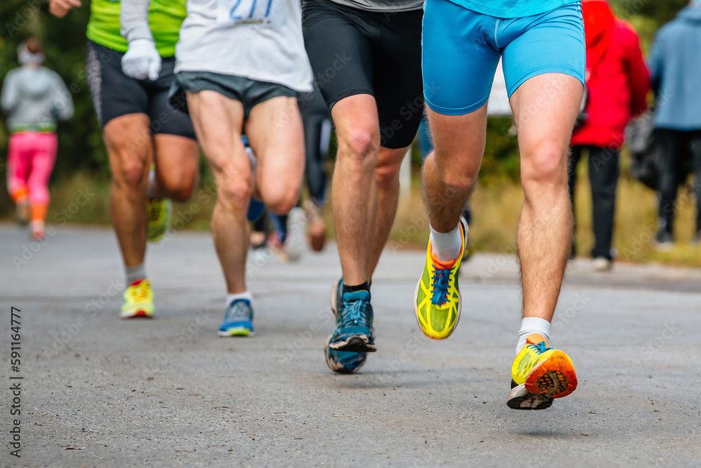 close-up legs group athletes runners running race on road, men jogging marathon