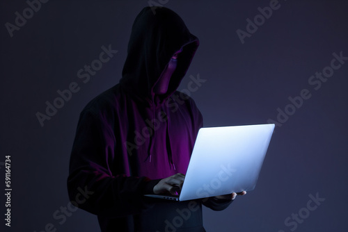 a hacker in a hoodie using a laptop computer isolated on dark background with neon light. Created with Generative AI Technology