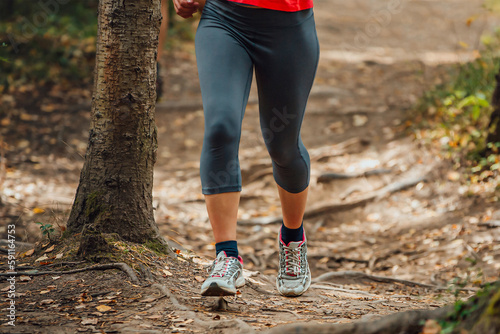 legs female runner in leggings runnin forest trail along roots of trees, summer marathon race