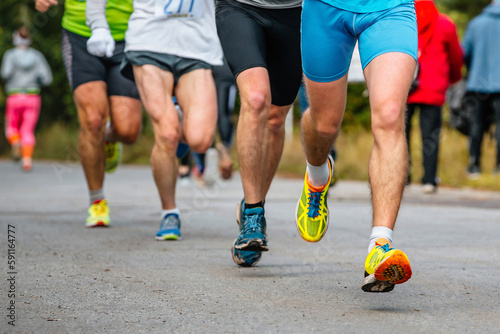 close-up legs group athletes runners running race on road, men jogging marathon