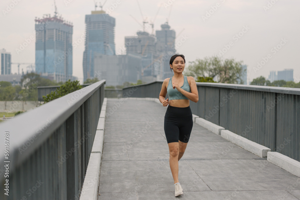 Asian happy woman running in park on morning. Healthy female wearing sportswear and warm-up exercise in outdoors. wellness lifestyle, outside activities.