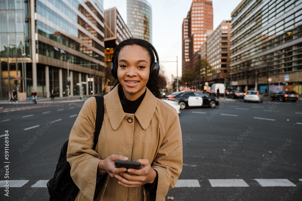 Fototapeta premium African girl listening music with headphones and smartphone while walking outdoors