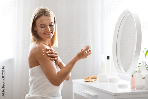 Skin Nourishing. Middle Aged Woman Applying Moisturising Cream On Shoulder At Home