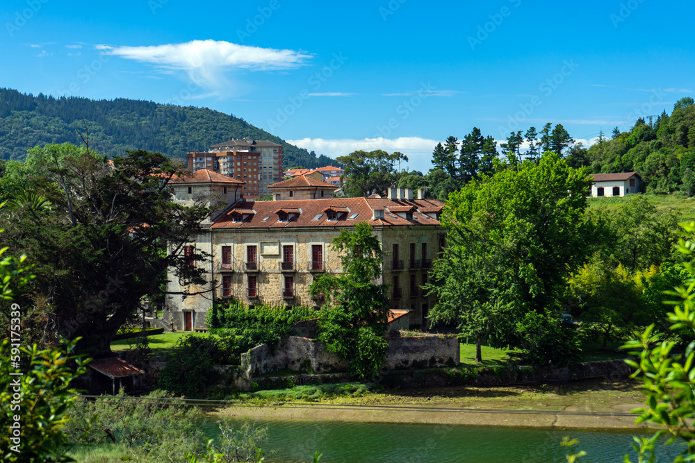 old manor house on river bank against background of high-rise buildings. Spain, Basque Country