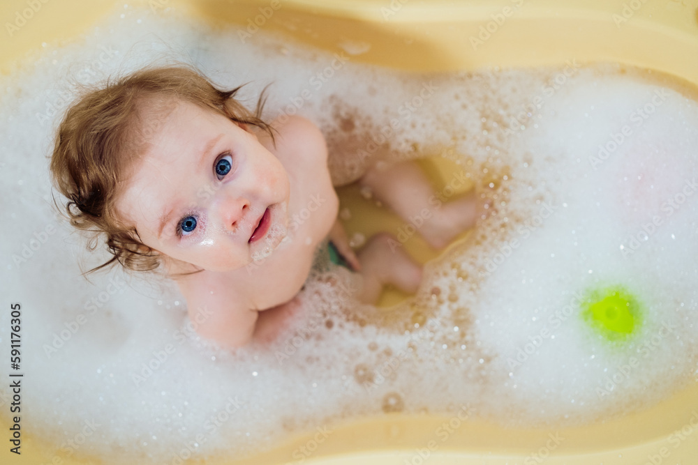 Baby girl in a bath with foam and soap bubbles. Happy laughing baby taking a bath playing with toys. Little child in a bathtub. Smiling kid in bathroom. Infant washing and bathing Baby girl in a bath with foam and soap bubbles. Happy laughing baby taking a bath playing with toys. Little child in a bathtub. Smiling kid in bathroom. Infant washing and bathing