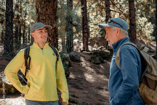 Smiling and Carefree Couple of Grandfather and young Grandson in Trekking Day Enjoying Nature and Healthy Lifestyle Together in the Woods. Adventureisageless