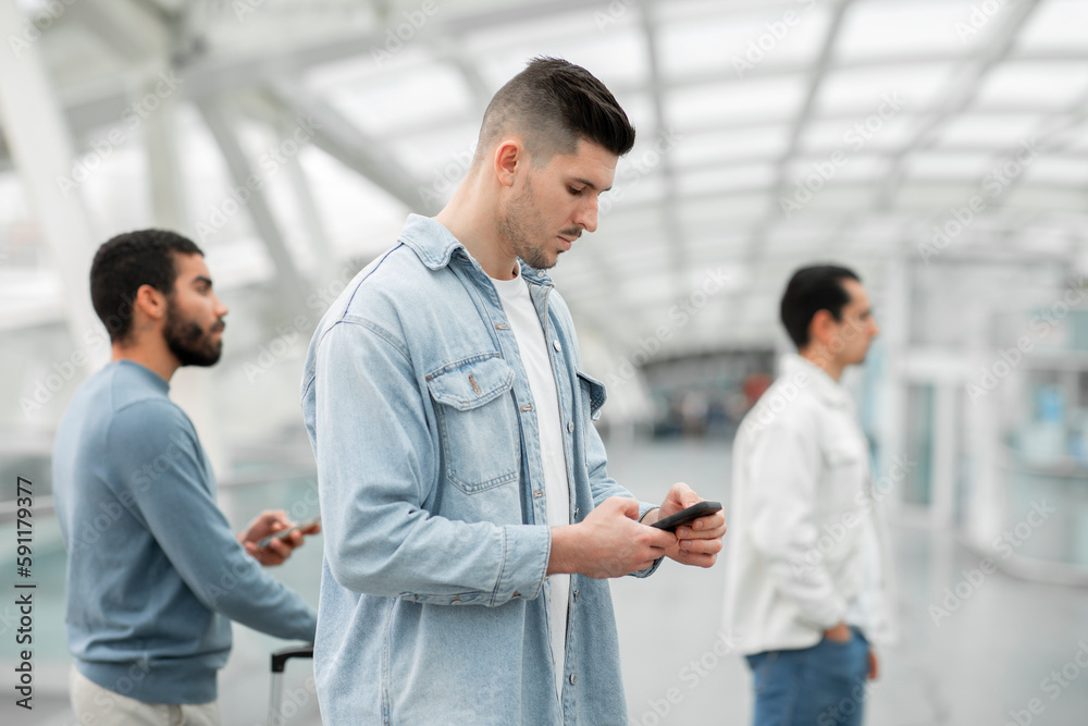 Man Using Smartphone Standing With Other Passengers In Modern Airport Man Using Smartphone Standing With Other Passengers In Modern Airport