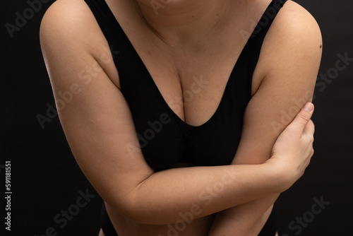 Female breast in black top closeup. Plump, plus size woman in sportswear. Flaunt figure imperfections. Studio portrait over black background. Concept of sport, body positive, self acceptance.