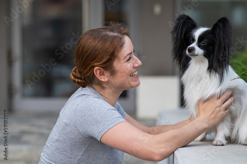 Caucasian red-haired woman cuddling with pappilion dog outdoors. Black and white continental spaniel. photo