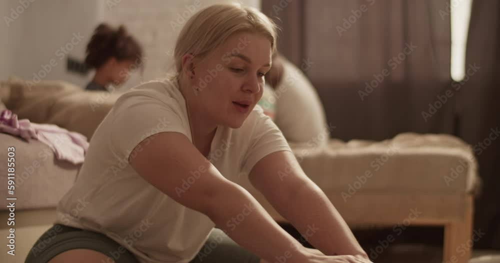 Tired woman training at home near black husband and kids playing on couch Tired woman training at home near black husband and kids playing on couch