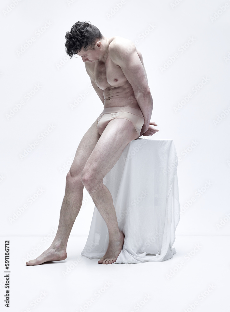Naklejka premium Full-length portrait of handsome man with attractive, strong, muscular body posing shirtless in underwear against white studio background. Male body aesthetics, men's beauty, inspiration, art concept