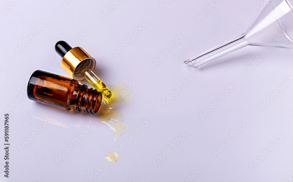 Laboratory studies. Dropper with drops of yellow liquid and glass amber cosmetic bottle on white background. Laboratory glass funnel. Natural organic cosmetics. Selective focus Laboratory studies. Dropper with drops of yellow liquid and glass amber cosmetic bottle on white background. Laboratory glass funnel. Natural organic cosmetics. Selective focus