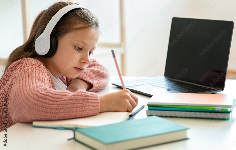Smart focused serious teenager european girl in headphones doing homework with laptop Smart focused serious teenager european girl in headphones doing homework with laptop
