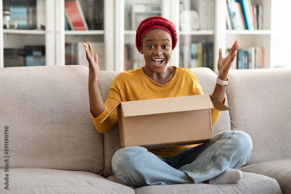 Emotional young black woman unpacking parcel at home, gesturing Emotional young black woman unpacking parcel at home, gesturing