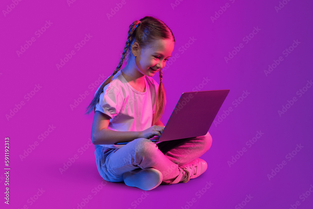 Cheerful cute preteen girl using laptop on colorful background