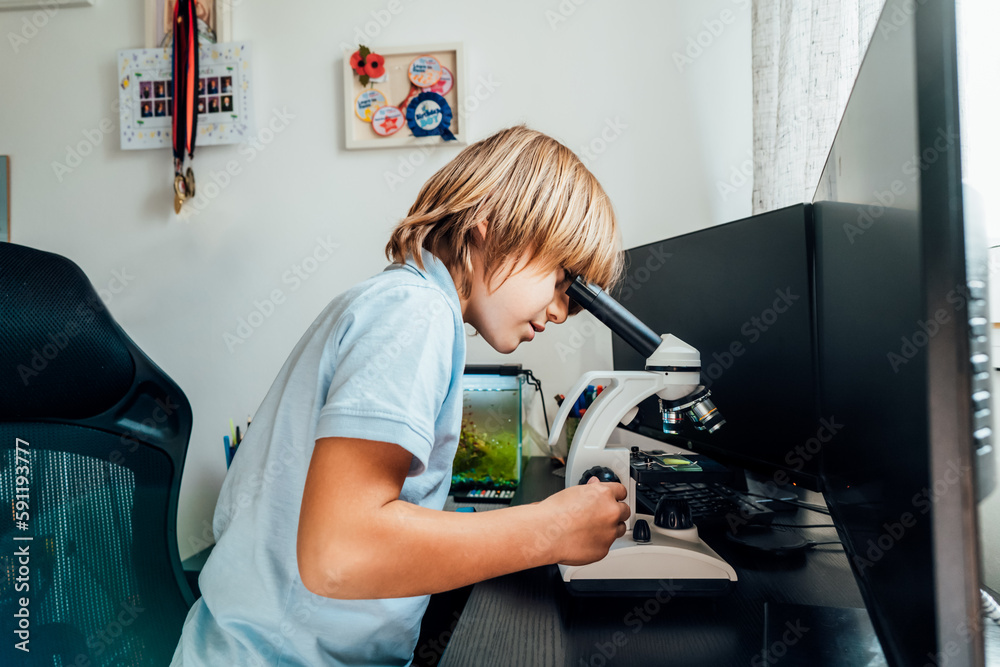 Caucasian boy using a microscope at home at his study place. Child curiosity, thirst for knowledge, home learning experience, home remote education concepts. Selective focus.
