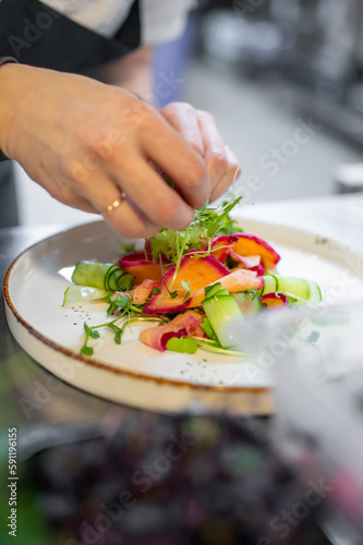 Chef cooking Green salad with salmon  cucumbers  lettuce  spices  caviar on restaurant kitchen