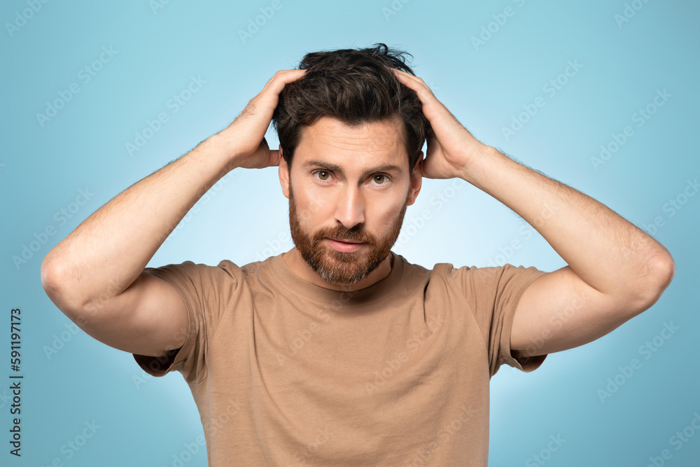 Portrait of handsome bearded middle aged man looking at camera and touching his hair, posing over blue background Portrait of handsome bearded middle aged man looking at camera and touching his hair, posing over blue background