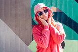 Urban Fresh street fashion. Mono color look. Vanilla Girl. Kawaii vibes. Candy colors design. Bucket hat trend. Young woman with pink hair and sun glasses in magenta sweatshirt on the wall background.