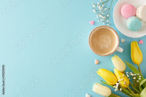Mother's Day concept. Top view photo of cup of coffee plate with macaroons small hearts yellow white tulips and gypsophila flowers on pastel blue background with blank space