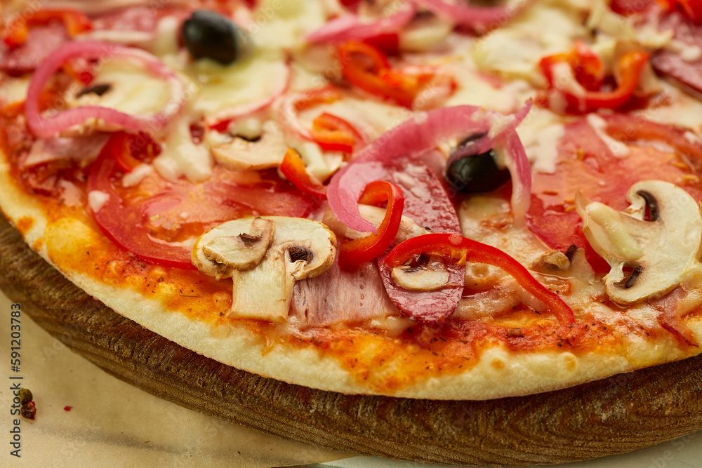 Freshly baked pizza with smoked sausages, red pepper, mushrooms, onion and olives served on wooden background with tomatoes, sauce and herbs. Food delivery concept. Restaurant menu