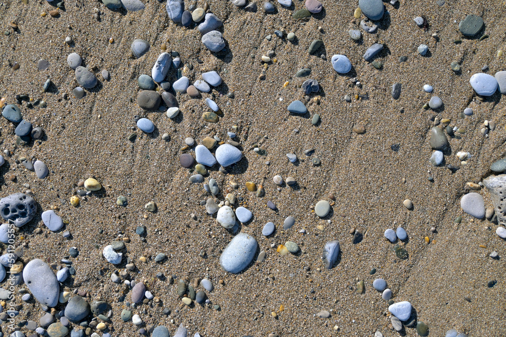 Piedras y cantos rodados de diferentes colores y tamaños sobre la arena de la playa al sol Piedras y cantos rodados de diferentes colores y tamaños sobre la arena de la playa al sol