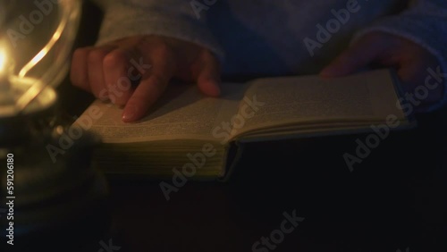 Female reading a book in the light of an kerosene lamp at night time, close up. Alternative light source concept. 