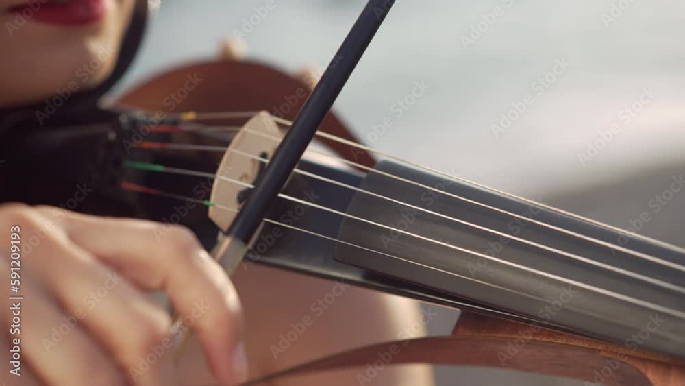 Close-up violin bow in female hands playing strings of musical instrument outdoors. Unrecognizable Caucasian talented lady enjoying music in sunshine Close-up violin bow in female hands playing strings of musical instrument outdoors. Unrecognizable Caucasian talented lady enjoying music in sunshine