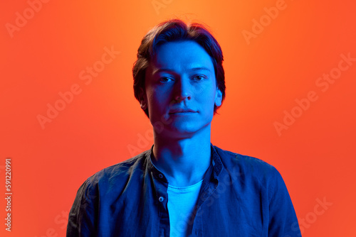 Portrait of young man, guy with calm face looking away over red-orange background in neon light. Concept of beauty, youth, human emotions, mood, ad © Lustre Art Group 