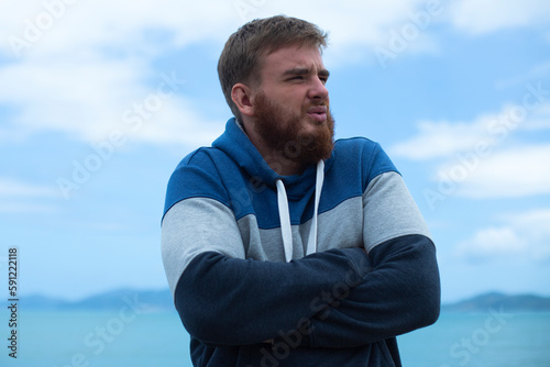 Portrait of unhappy depressed frozen trembling guy, young shivering from cold sad upset man on the sea beach, suffering from bad weather on summer vacation 