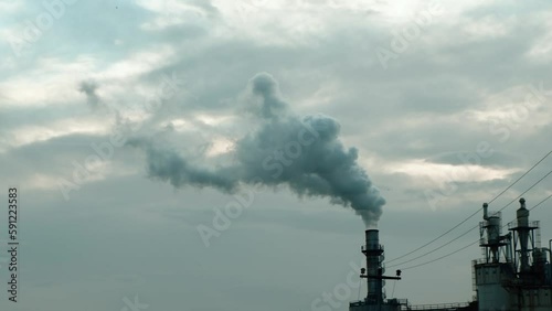Steam and smoke coming out of a factory chimney against a cloudy sky. Air pollution concept, emissions, station, climate change, global warming, oil refinery, industry