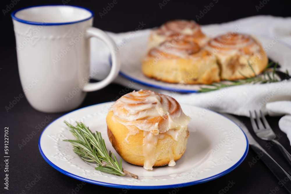 homemade cinnamon rolls on white ceramic plates decorated with rosemary and a cup of tea