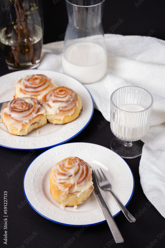 cinnamon rolls on white plate with blue rim decorated with rosemary and jug of milk