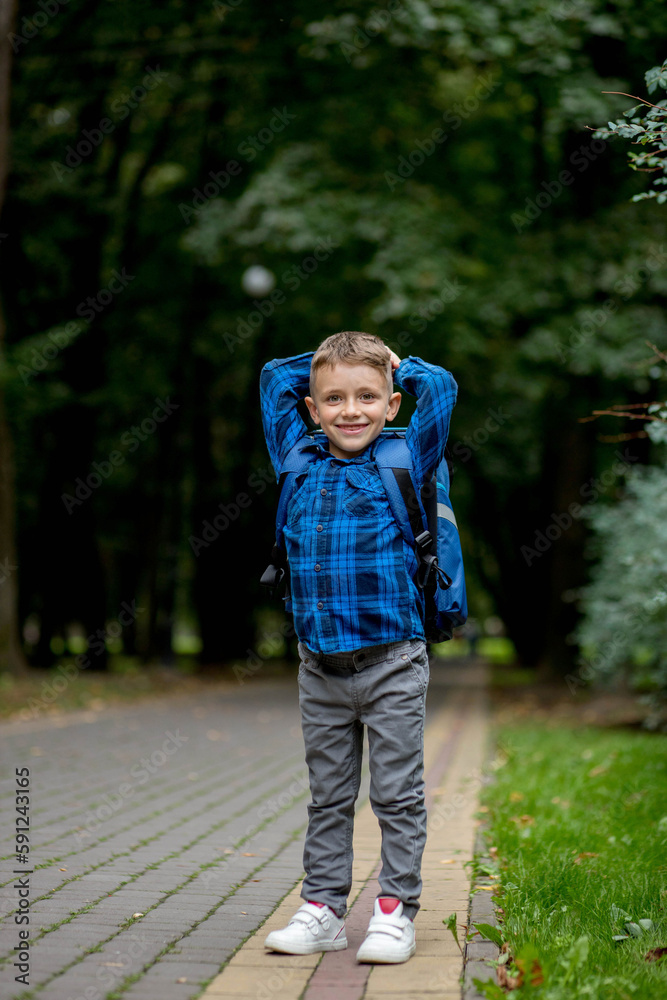 Fototapeta premium Boy of school age with a blue backpack goes to school in the park