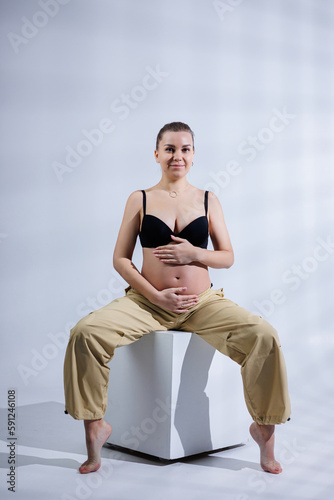 Young happy pregnant woman in bra and pants on white background. Happy pregnancy. Stylish pregnant woman poses in the studio